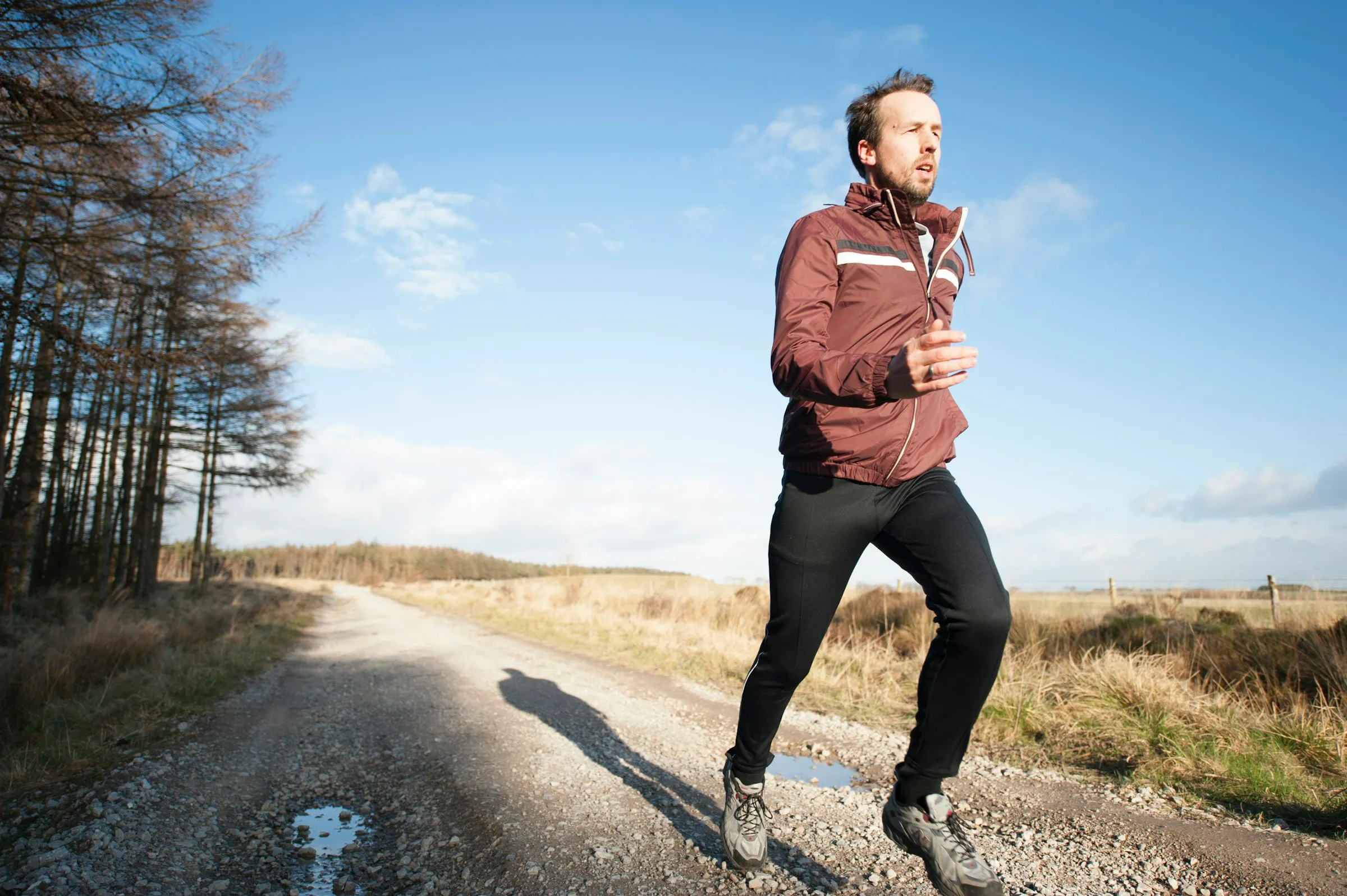A man running on a gravel path under a blue sky